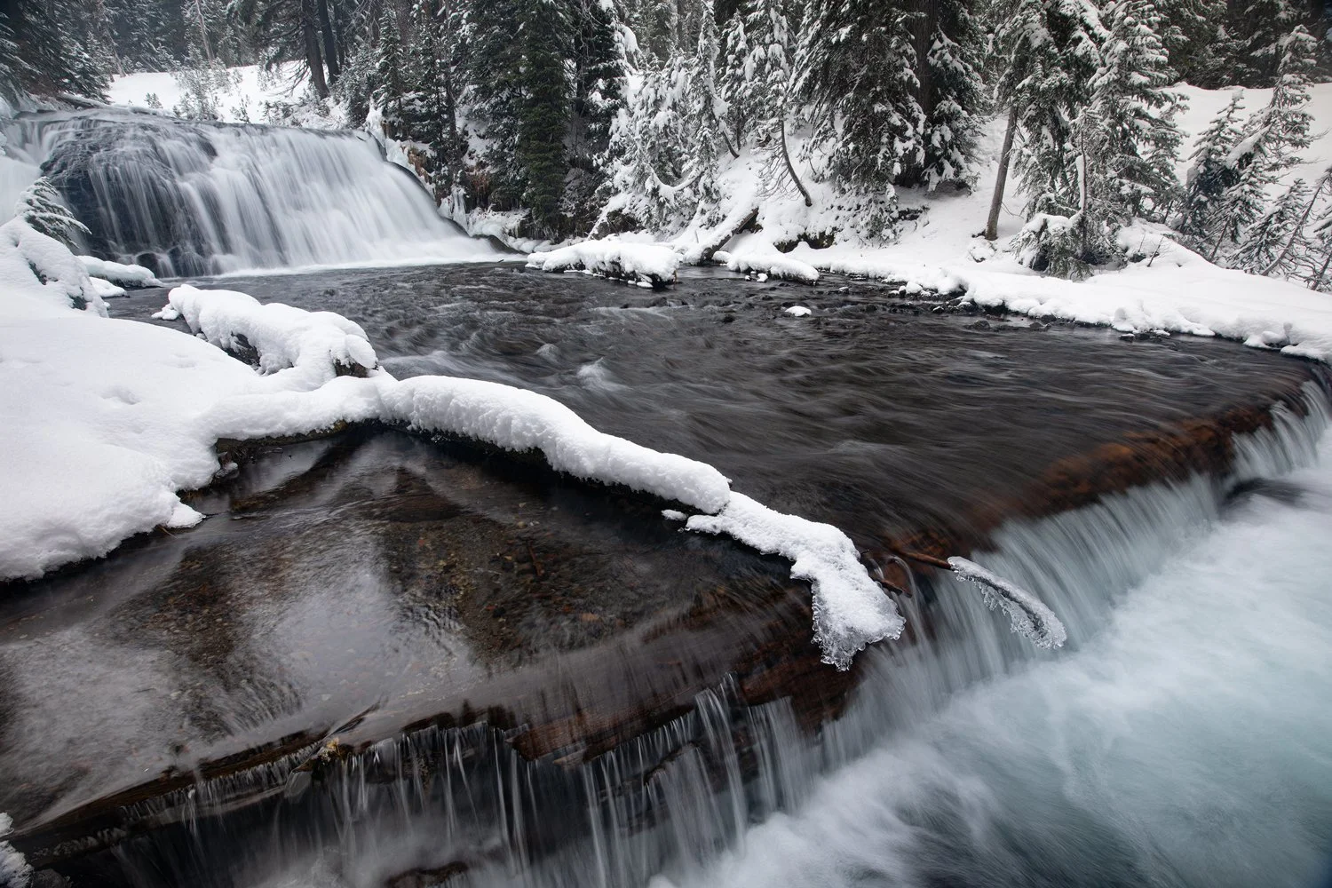 Snow Creek Falls flowing past ice-crusted rocks in a snowy forest
