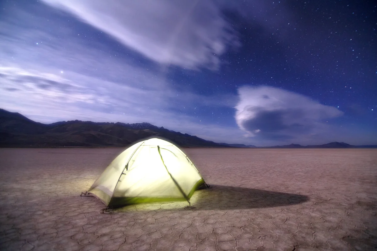 Glowing tent pitched on the Alvord Desert playa under a starry night sky