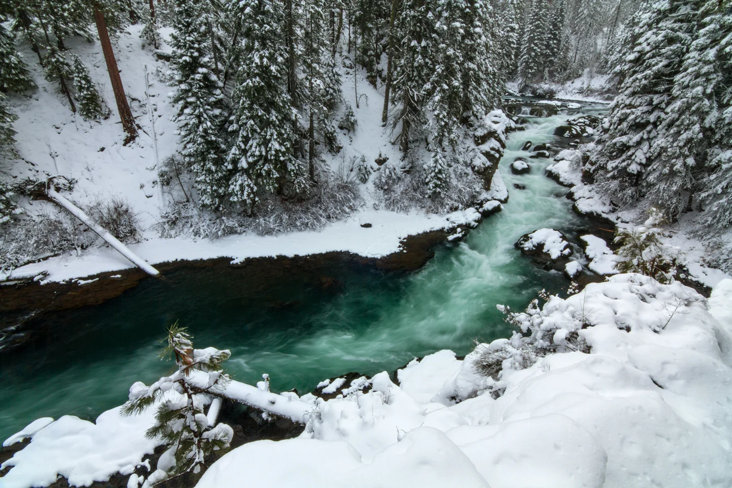 Benham Falls' turquoise water rushing through a snow-covered forest canyon