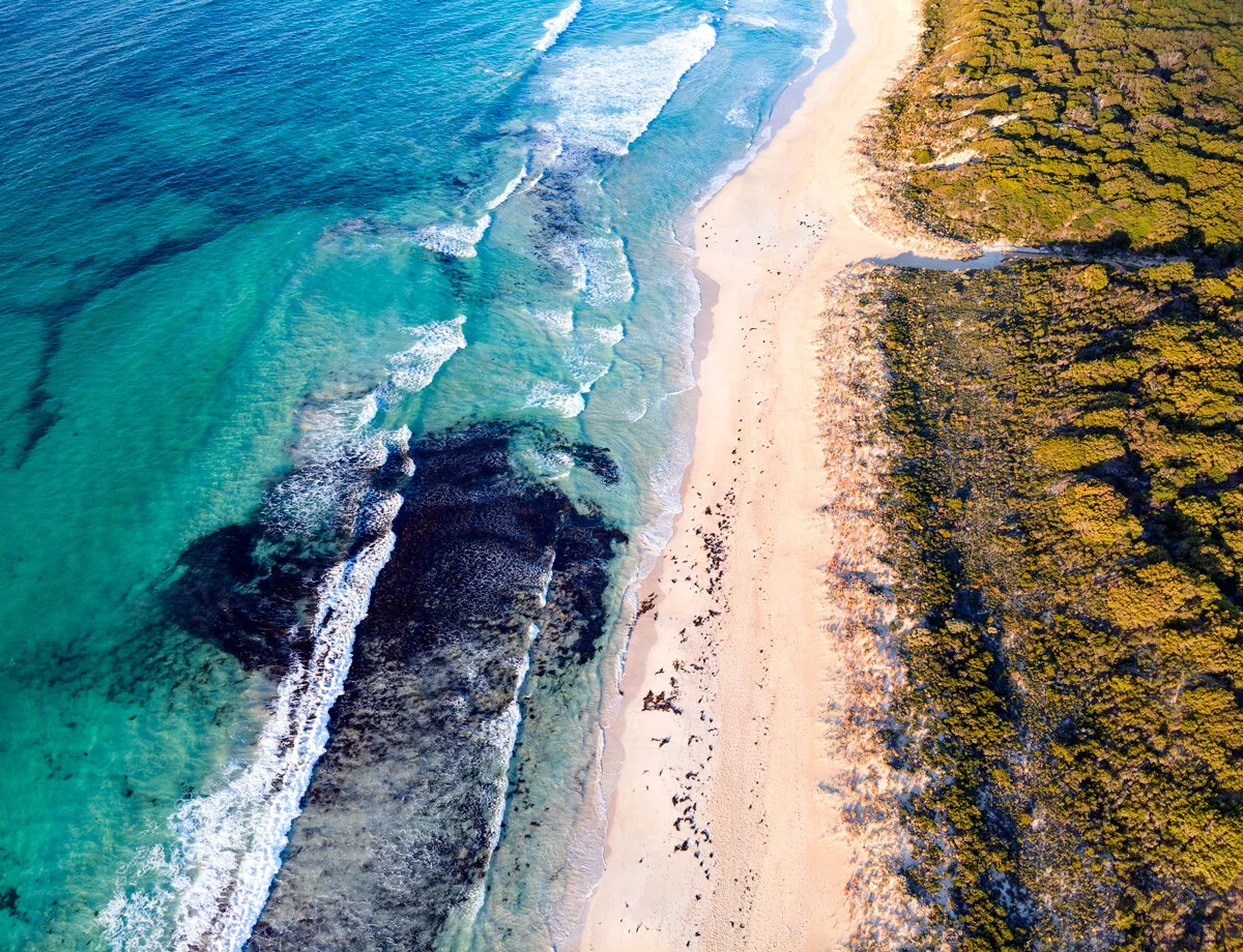 Aerial view of turquoise waves rolling into Bunker Bay's reef-lined shore