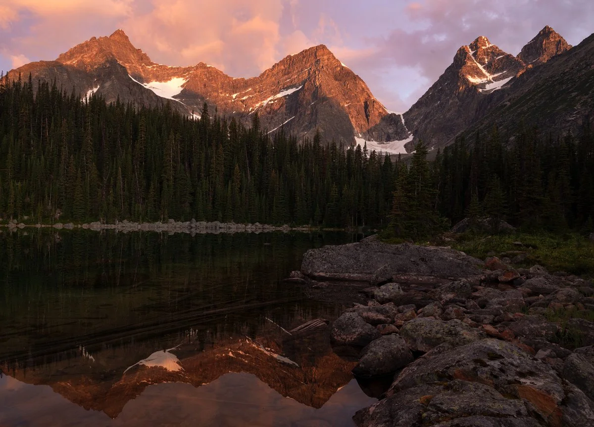 Canadian Rockies range glowing pink at sunset above a mirror lake