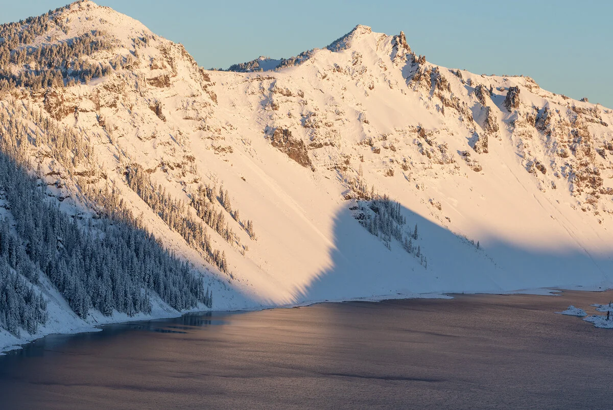 Crater Lake's snow-covered rim casting a shadow over the water in winter