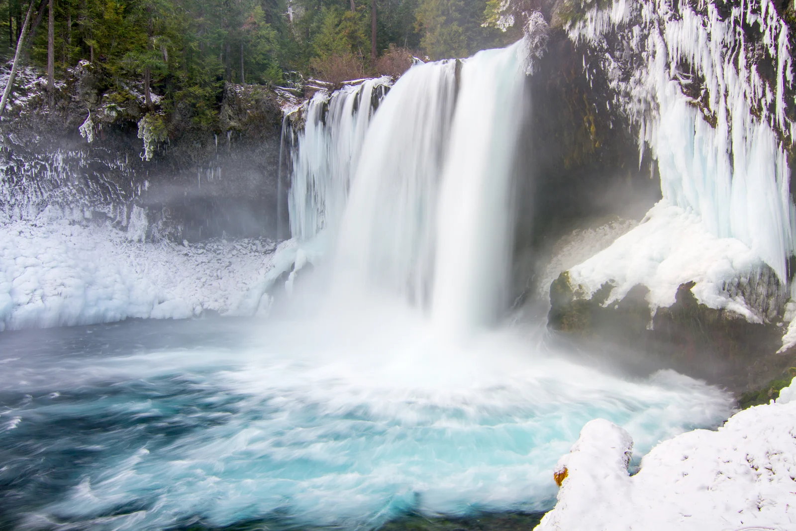 Koosah Falls thundering into a turquoise pool with icy rocks in winter