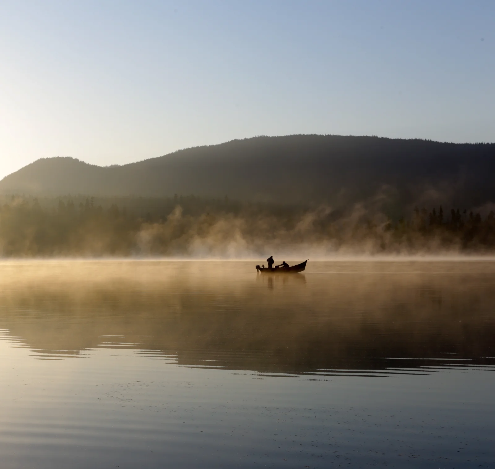 Two anglers fishing from a boat on a misty lake at sunrise