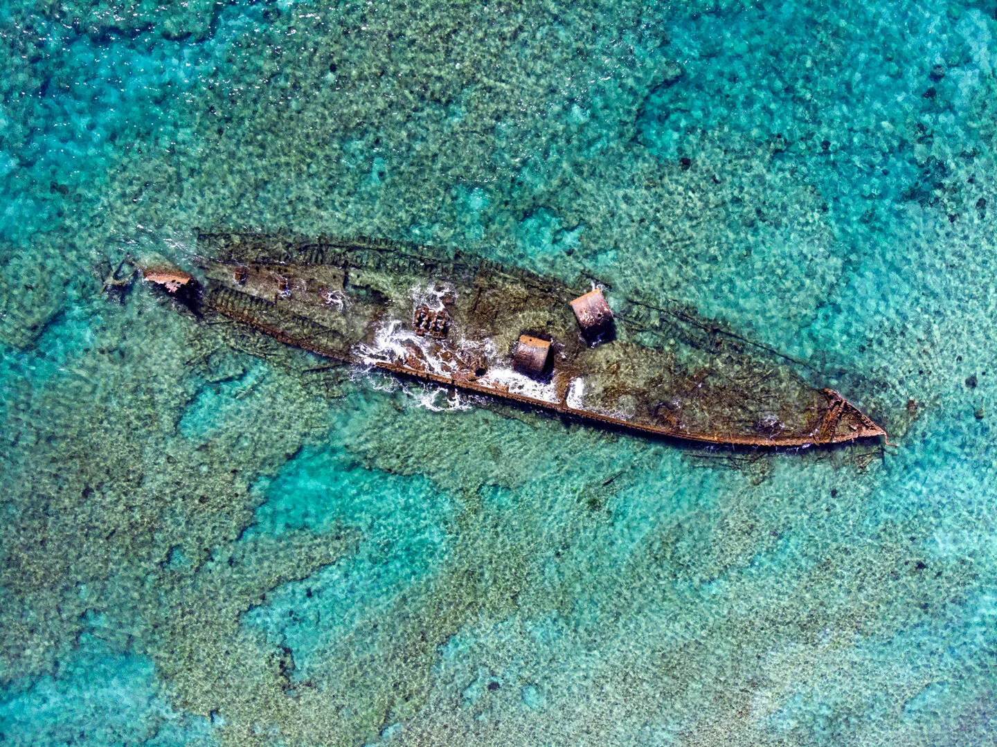 Aerial view of a rusted shipwreck resting in shallow turquoise reef water