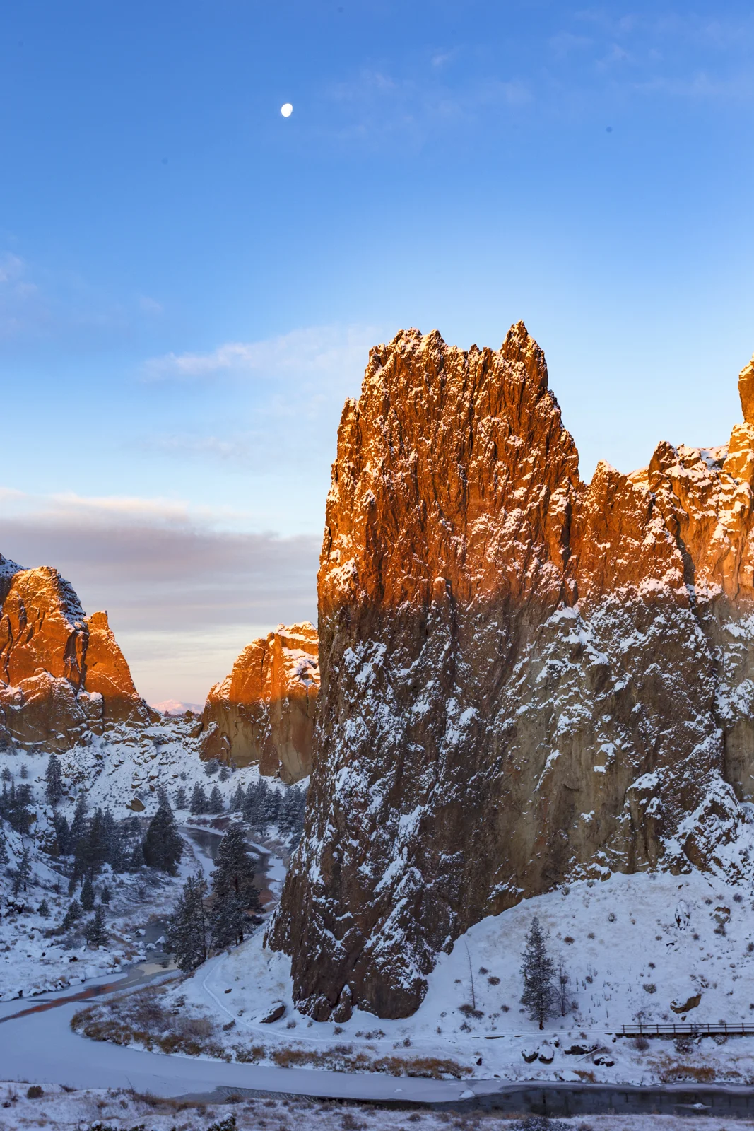 Smith Rock's sunlit spire rising above a snowy canyon with the moon overhead