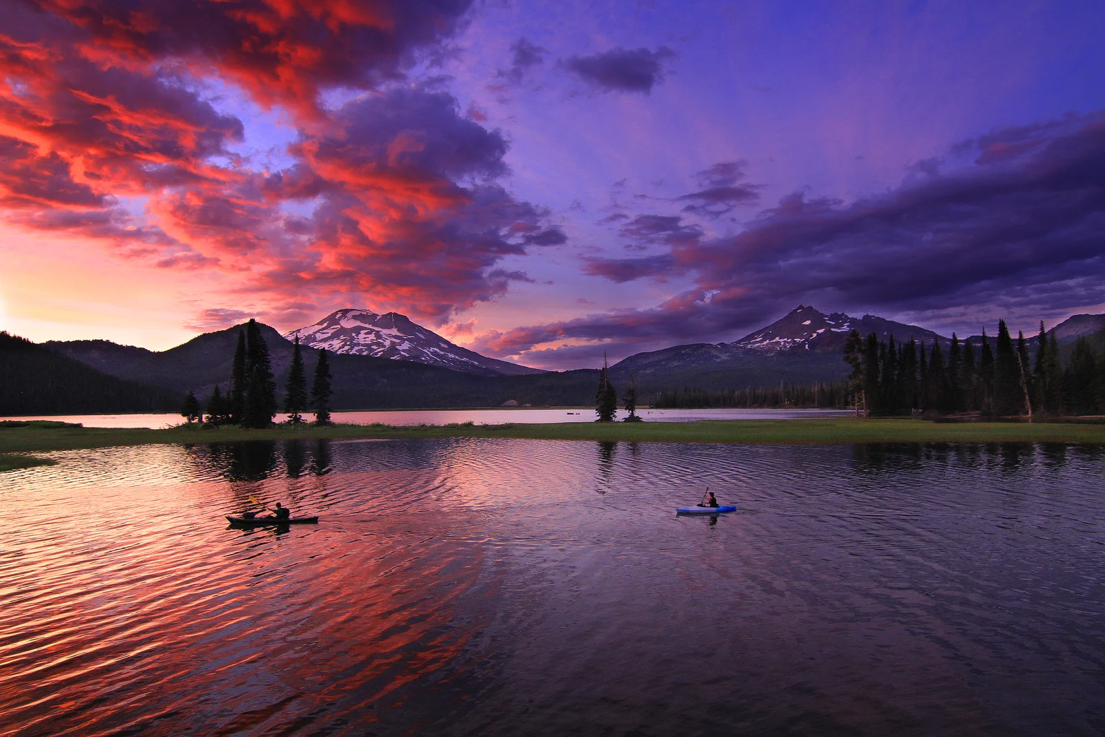 Kayakers paddling Sparks Lake beneath fiery clouds and snow-capped peaks at sunset
