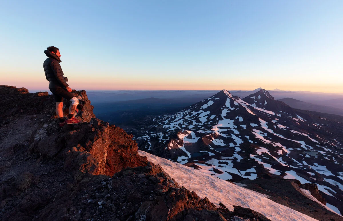 Hiker admiring snow-patched Cascade peaks at dusk from South Sister