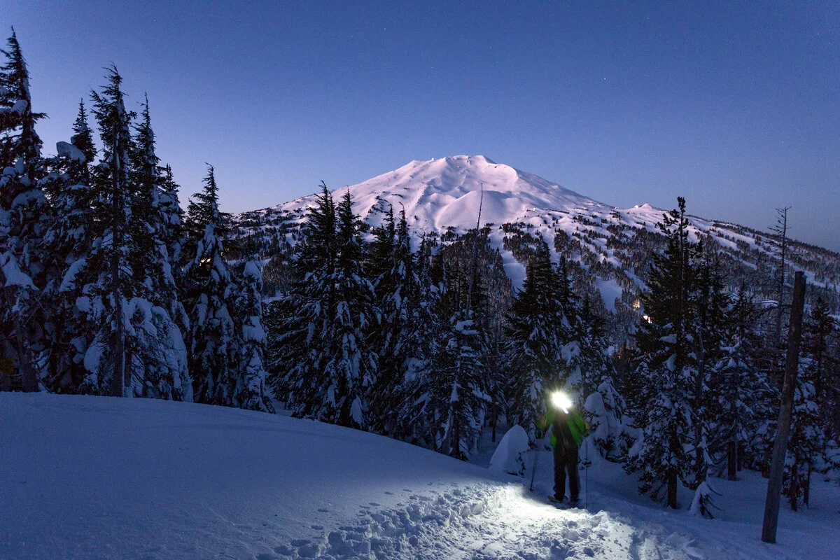 Snowshoer's headlamp glowing beneath Mount Bachelor at dusk